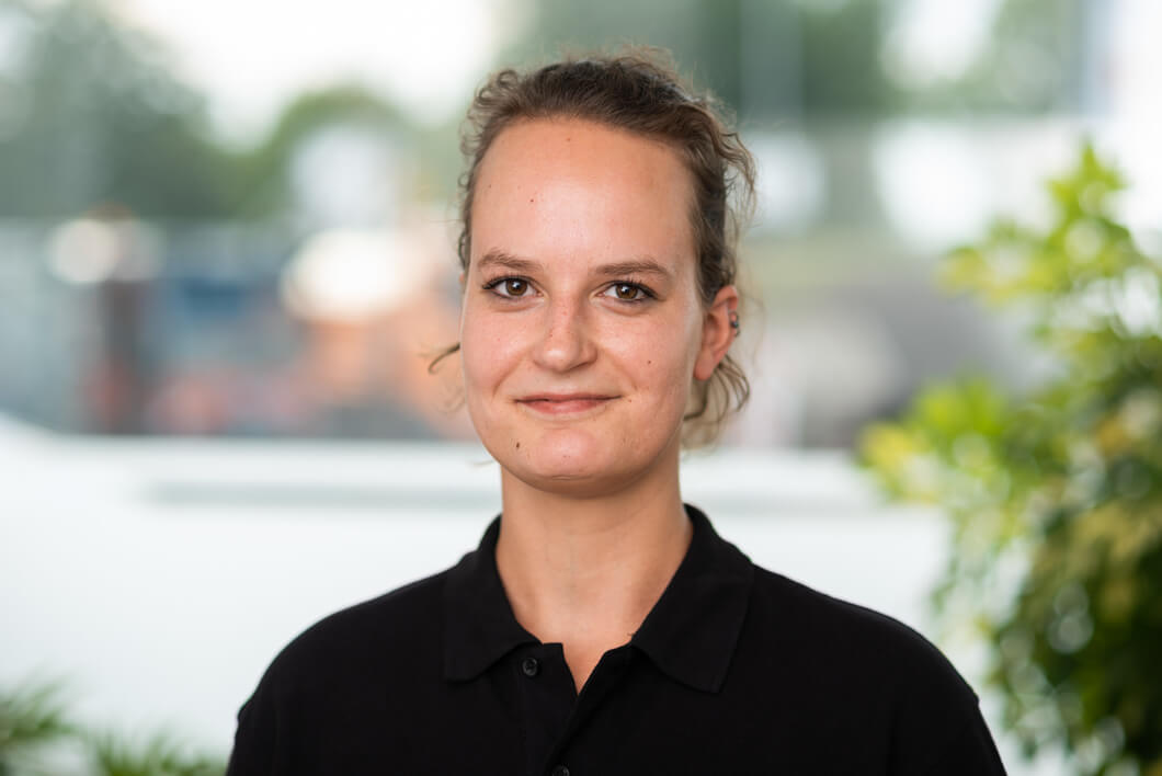 Constanze Malsch – Business Assistant to CEO Porträt einer freundlich lächelnden Mitarbeiterin mit hochgebundenen braunen Haaren und schwarzem Poloshirt vor einem hellen Hintergrund.