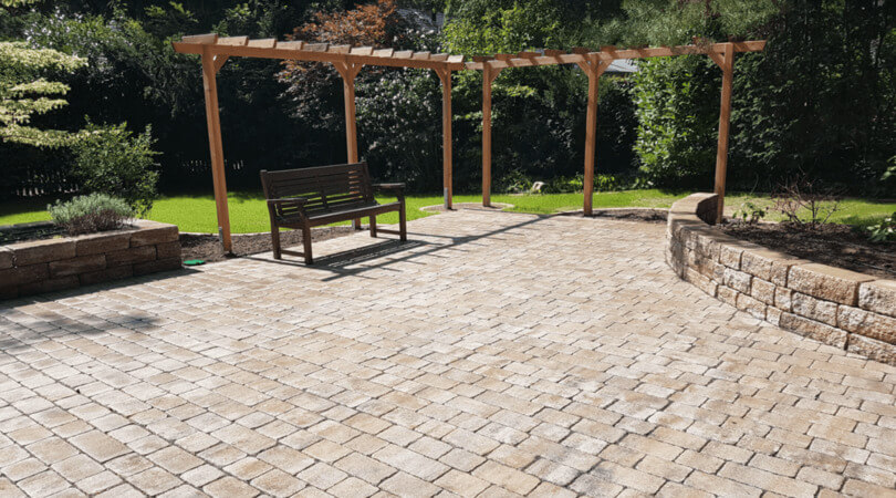 Große gepflasterte Terrasse mit Holzpergola und Sitzbank im Privatgarten.