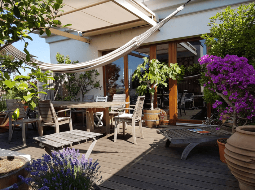 Begrünte Dachterrasse mit Gartenmöbeln und blühenden Pflanzen – STRAMAN Begrünte Dachterrasse mit Holzmöbeln, Hängematte, blühendem Lavendel und violetten Blüten als Beispiel für moderne Terrassengestaltung.