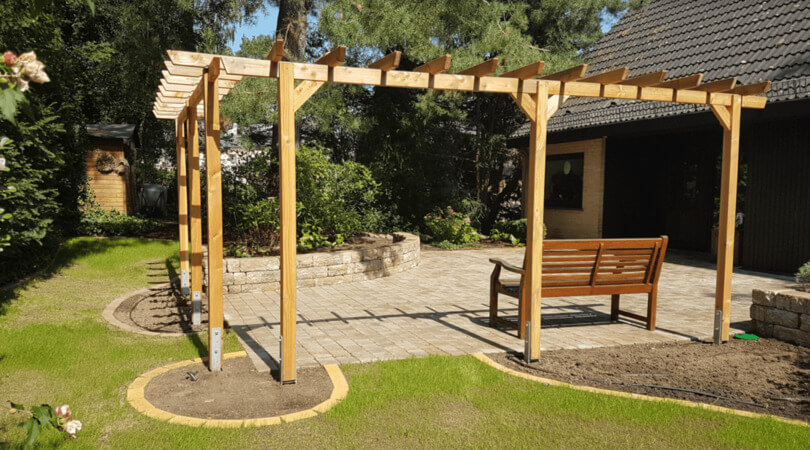 Moderne Holzpergola mit Sitzbank auf gepflasterter Terrasse in gepflegtem Privatgarten.