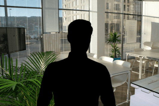 STRAMAN Mitarbeiter Schwarze Personensilhouette vor einem modernen, lichtdurchfluteten Büro mit Glaswänden, Besprechungstischen und Grünpflanzen.