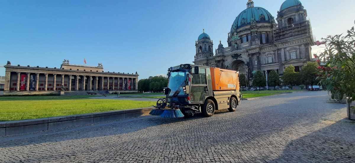 Orangefarbene Kehrmaschine auf einem Platz vor dem Berliner Dom.