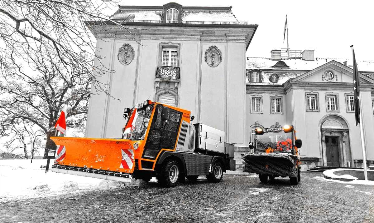 Straman – Winterdienst Berlin Winterdienstfahrzeuge der Firma STRAMAN mit Schneepflug und Kehrbürste vor historischer Schlossanlage in Berlin.
